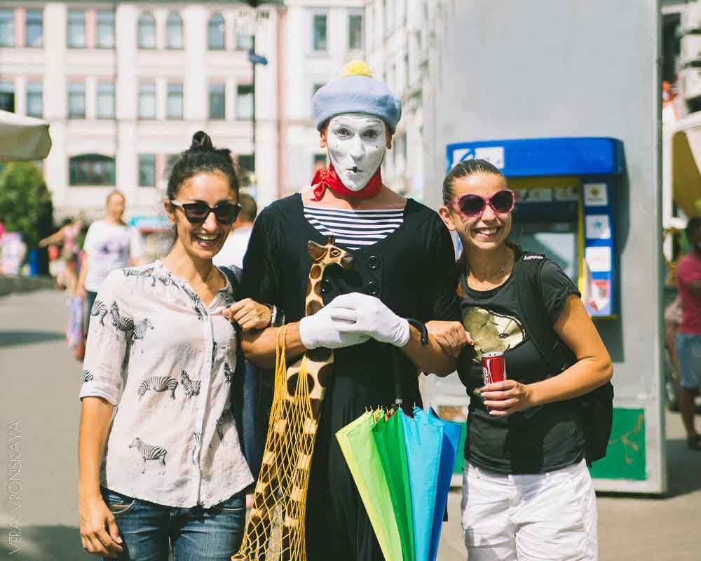 Giraffe war nur der Anfang. Französischer Pantomime-Künstler mit Holz-Giraffe und lachenden Frauen.