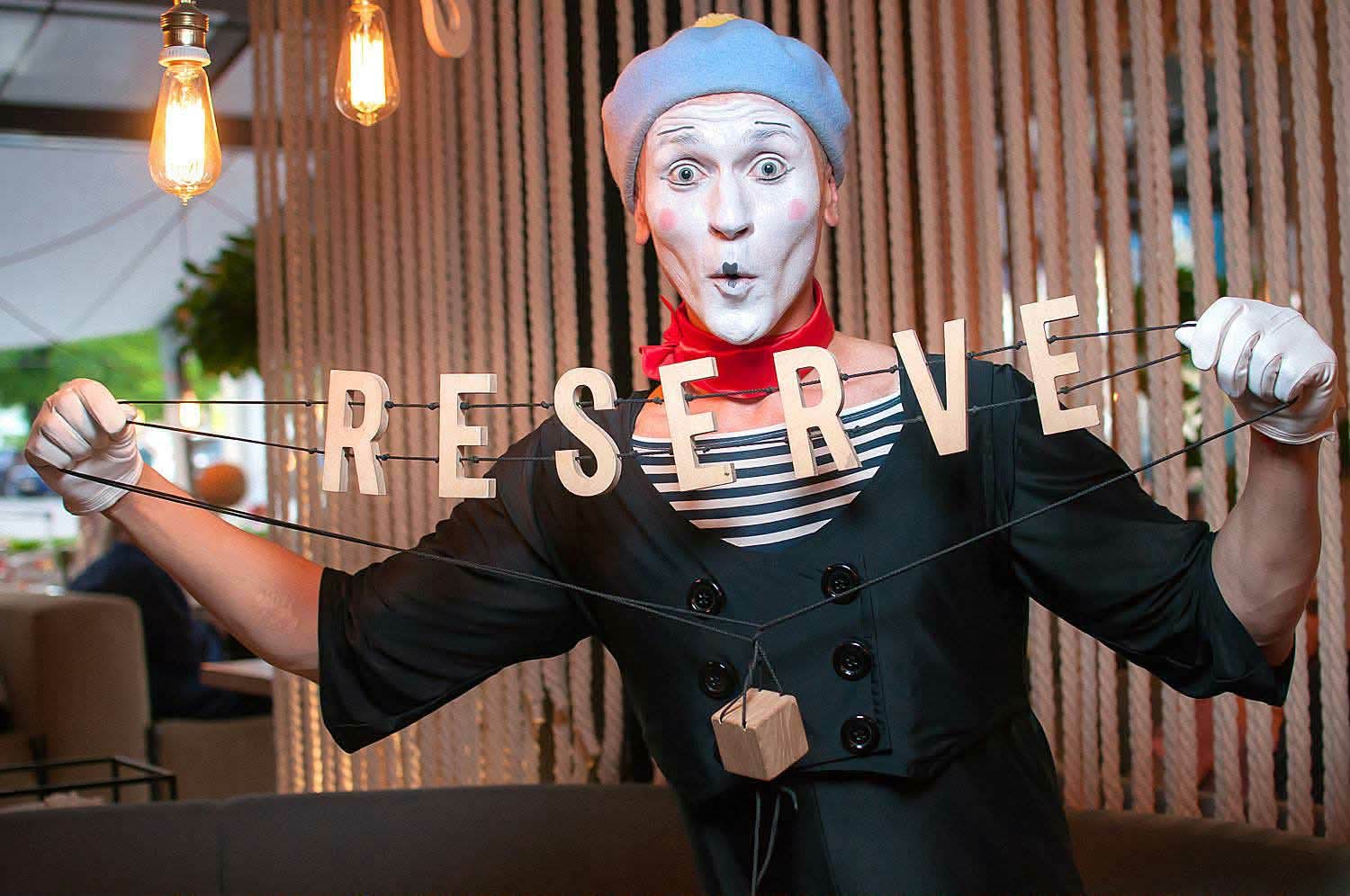 Reserviert. Aber mit Stil. Französischer Pantomime-Künstler mit Reserviert-Schild im Restaurant im Berlin